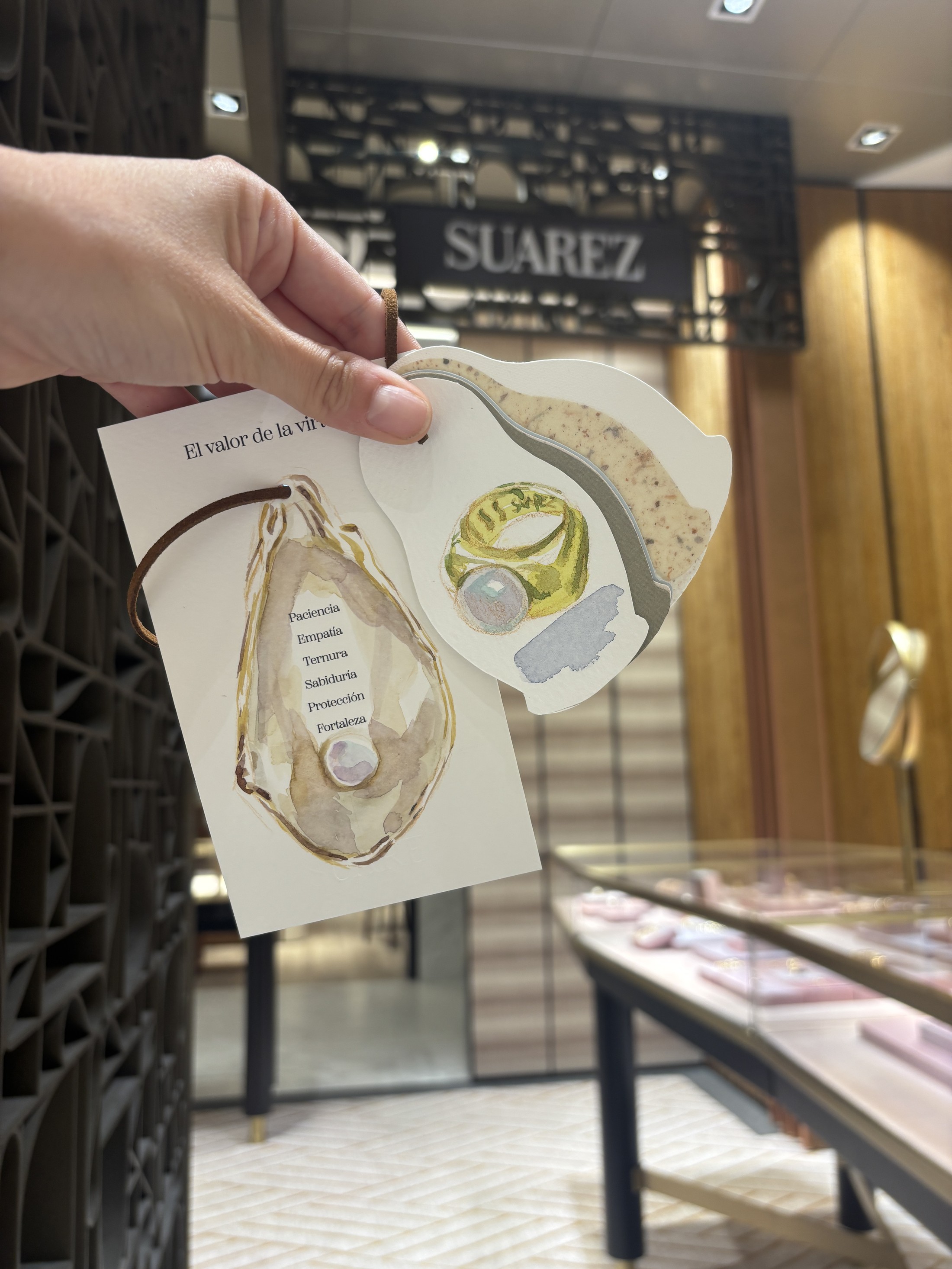 Tarjeta pintada en directo con un anillo, junto al rótulo de la joyería Suárez