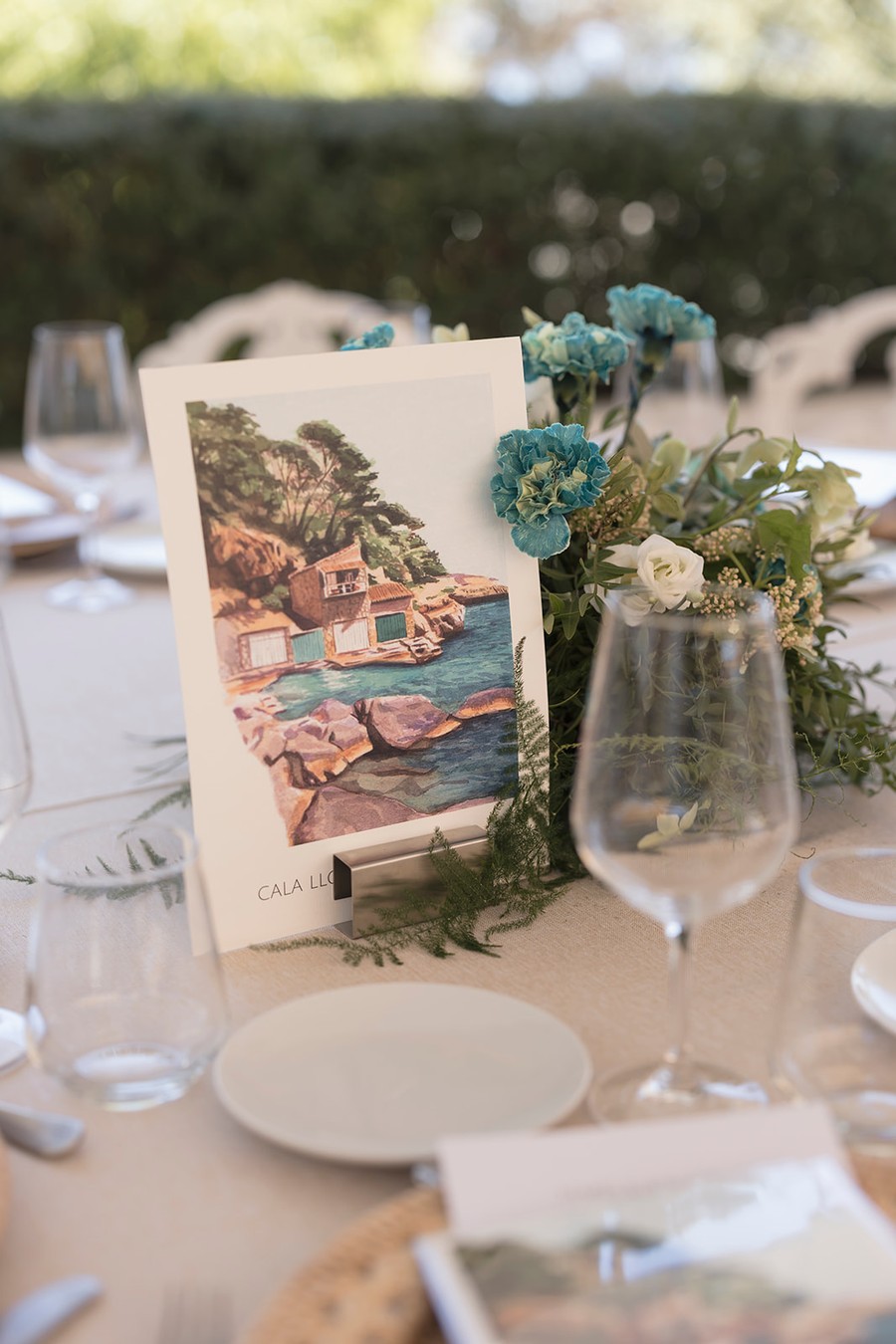 Mesero de boda con una acuarela de una cala mallorquina junto al centro de flores