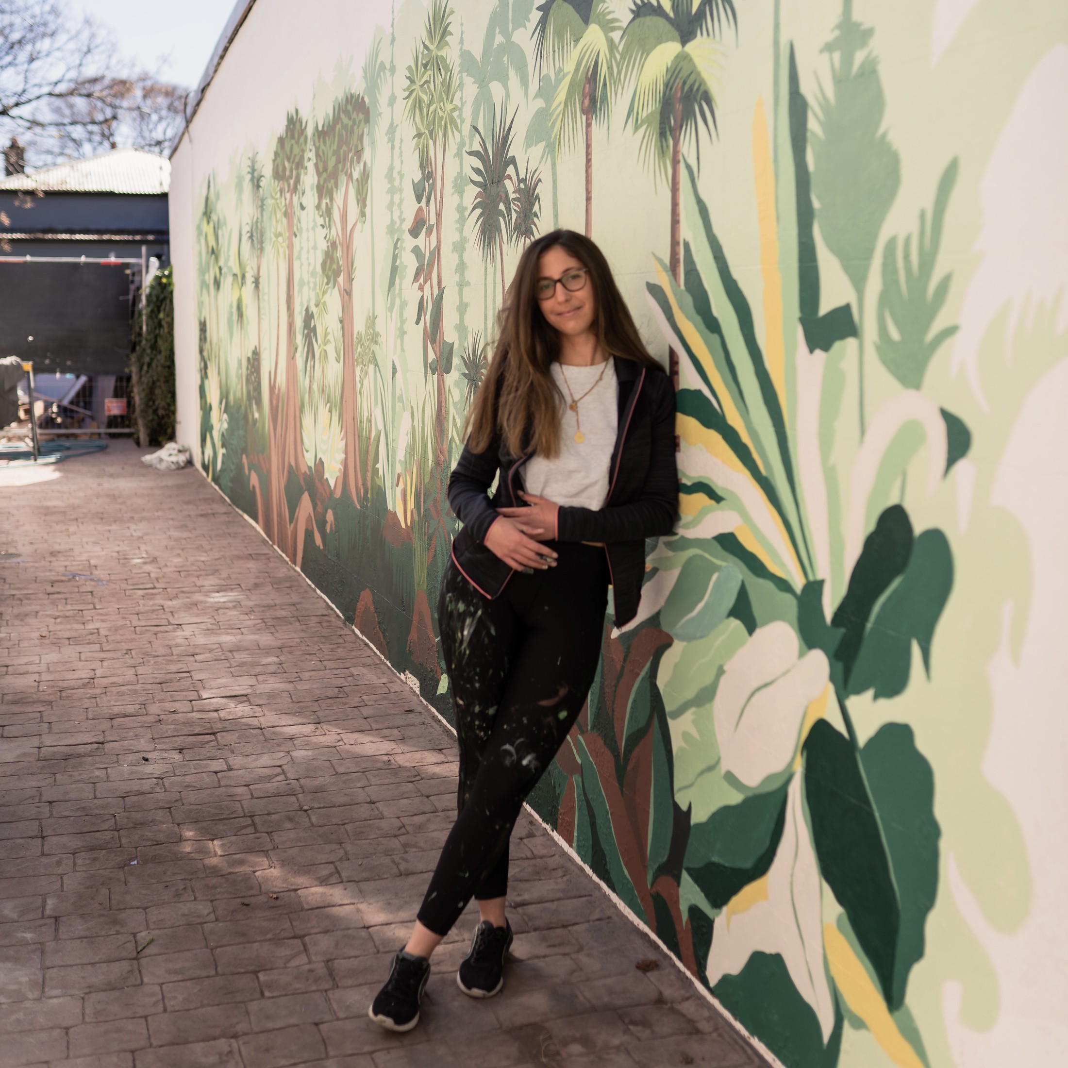Mural botánico de gran formato con palmeras, María Téllez posando delante para apreciar la escala