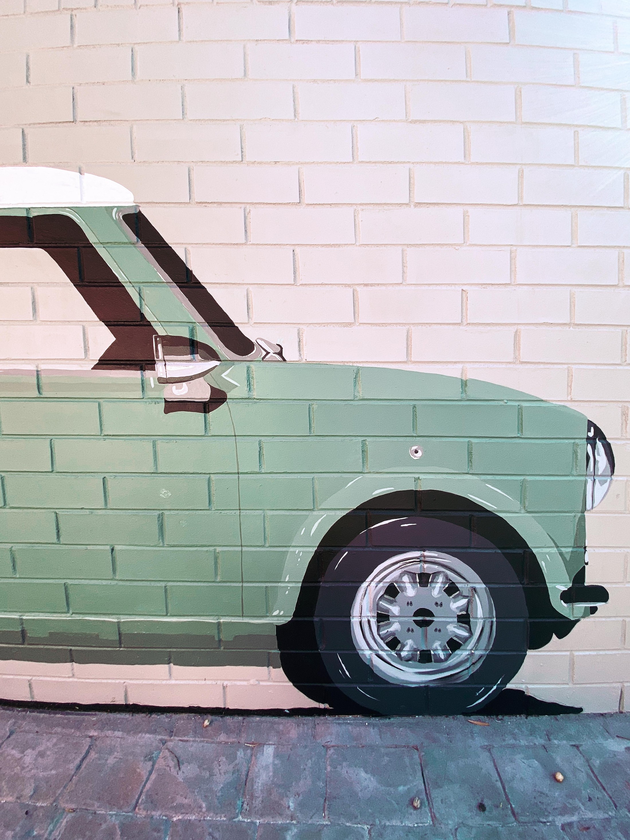 Mural realista de un Mini Cooper verde pintado a tamaño real sobre pared de ladrillo