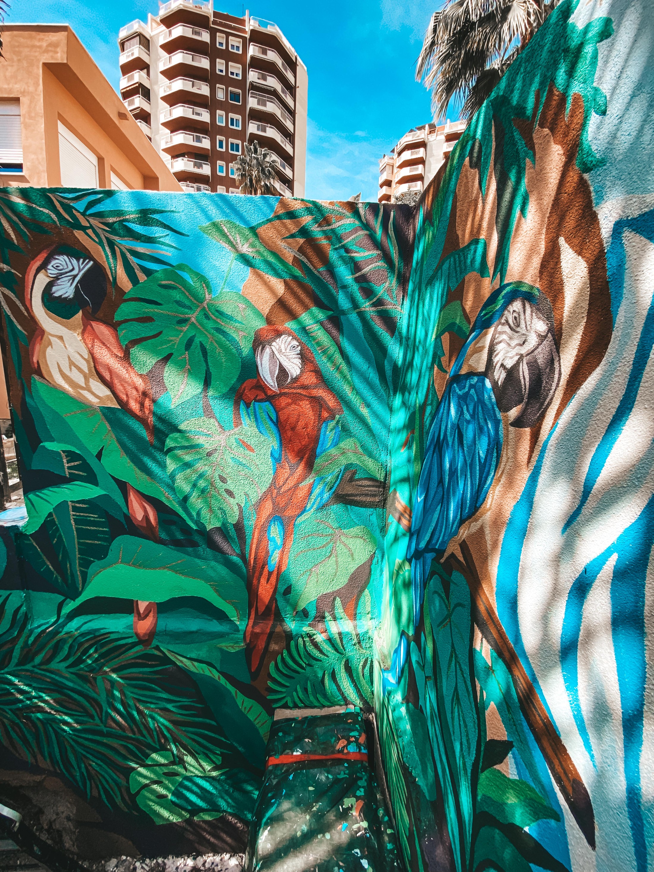 Mural tropical con loros y vegetación exuberante en tonos verdes y azules